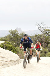 Smiling couple riding bicycles on rocks against clear sky - CAVF31209