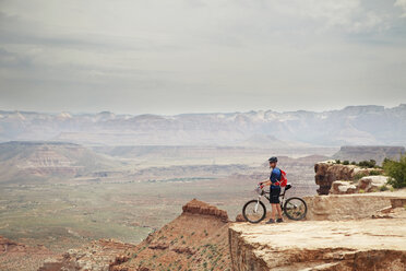 Man standing with bicycle on cliff against mountains - CAVF31212