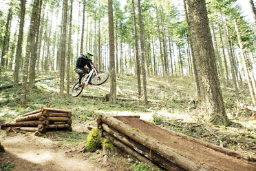 Niedriger Blickwinkel auf einen Mann, der einen Stunt mit einem Fahrrad im Wald macht - CAVF31242