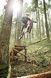 Low angle view of man jumping with bicycle against trees - CAVF31243