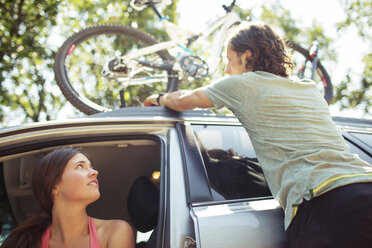 Woman looking at man standing by car with bicycle on roof - CAVF31254