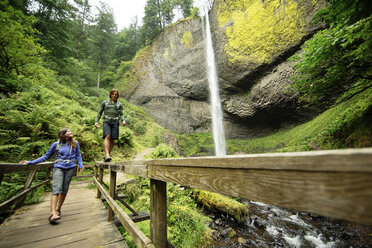 Couple walking on footbridge by waterfall in forest - CAVF31255