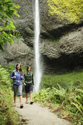 Paar, das auf einem Fußweg bei einem Wasserfall im Wald spazieren geht - CAVF31257