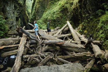 Couple walking on logs amidst rock formations in forest - CAVF31259