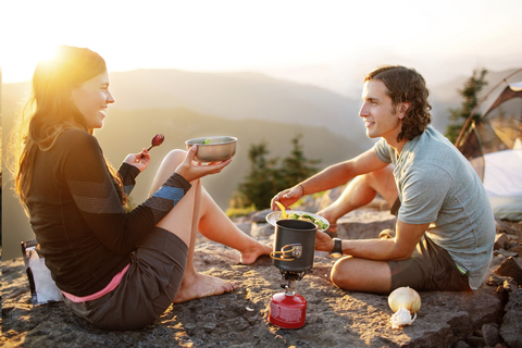 Glückliches Paar beim Essen auf dem Berg sitzend gegen den klaren Himmel, lizenzfreies Stockfoto