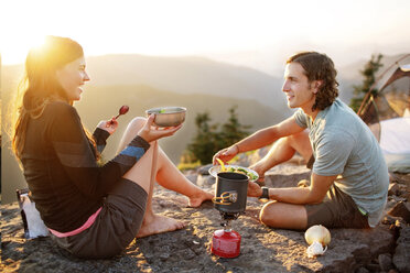 Glückliches Paar beim Essen auf dem Berg sitzend gegen den klaren Himmel - CAVF31268