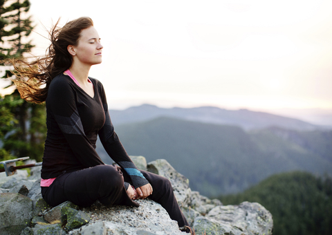 Frau meditiert auf einem Felsen sitzend gegen den klaren Himmel, lizenzfreies Stockfoto