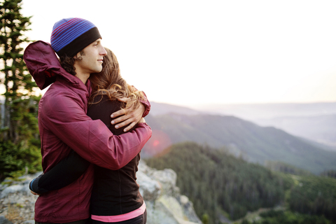 Paar, das sich umarmt, während es auf dem Gipfel eines Berges gegen den klaren Himmel steht, lizenzfreies Stockfoto