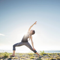 Woman practicing extended side angle pose yoga at beach during sunny day - CAVF31299