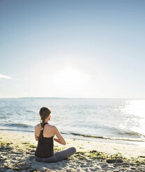Rückansicht einer meditierenden Frau am Strand gegen den Himmel an einem sonnigen Tag - CAVF31301