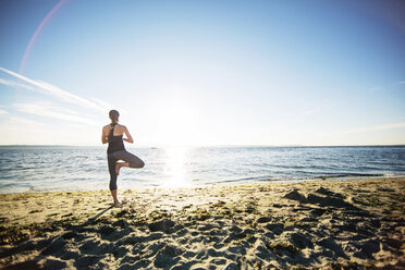 Rückansicht einer Frau in Baumpose am Strand an einem sonnigen Tag - CAVF31303
