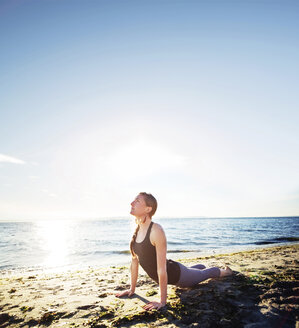 Frau übt Kobra-Pose am Strand gegen den Himmel an einem sonnigen Tag - CAVF31304