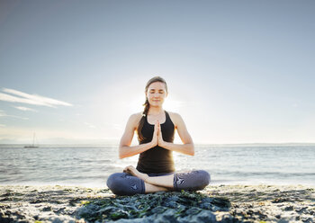 Woman meditating in lotus position at beach against sky - CAVF31306