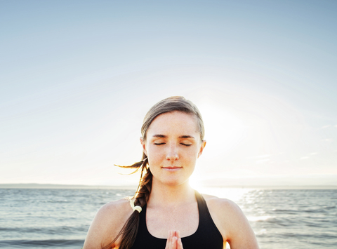 Woman meditating in lotus position by sea against sky stock photo