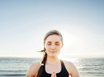 Woman meditating in lotus position by sea against sky - CAVF31307