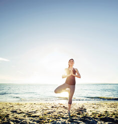 Frau meditiert in Baumpose am Strand gegen den Himmel - CAVF31308