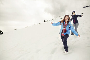 Fröhliche Freundinnen laufen auf einem schneebedeckten Berg vor einer Wolkenlandschaft - CAVF31314