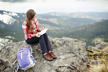 Lächelnde Frau, die auf einem Berg sitzend eine Zeitung liest - CAVF31321