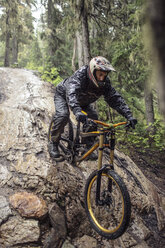 Mann beim Mountainbiking auf umgestürztem Baumstamm im Wald - CAVF31327