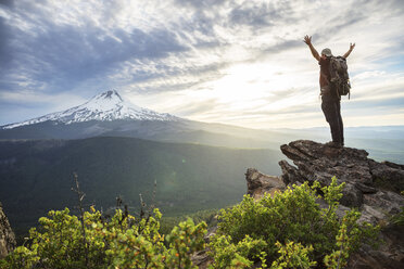 Hiker with arms outstretched standing on mountain against cloudy sky - CAVF31328