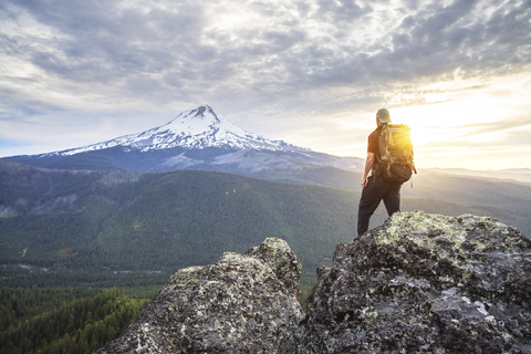 Rückansicht eines Wanderers, der auf einem Berg stehend die Aussicht gegen den bewölkten Himmel betrachtet, lizenzfreies Stockfoto