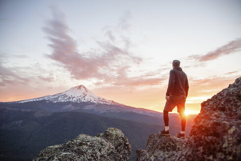 Rückansicht eines Wanderers, der bei Sonnenuntergang auf einem Berg steht und die Aussicht betrachtet - CAVF31335