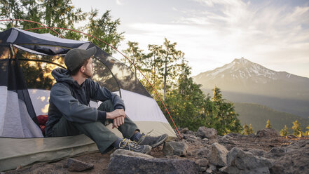 Male hiker looking away while sitting in tent against sky - CAVF31340