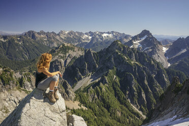 Wanderer, der die Aussicht betrachtet, während er auf einem Berg gegen den klaren Himmel an einem sonnigen Tag sitzt - CAVF31348