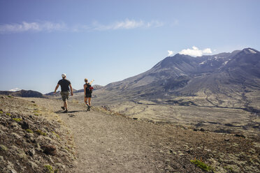 Rear view of friends hiking on landscape against sky during sunny day - CAVF31357