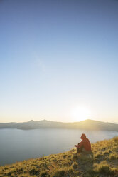 Wanderer sitzt auf einem Berg im Crater Lake National Park gegen den klaren Himmel bei Sonnenuntergang - CAVF31363
