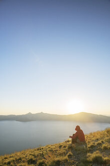 Wanderer sitzt auf einem Berg im Crater Lake National Park gegen den klaren Himmel bei Sonnenuntergang - CAVF31363