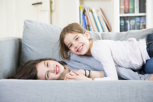 Porträt von zwei glücklichen Schwestern, die auf der Couch kuscheln - LVF06839
