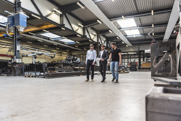 Three men with tablet walking and talking on factory shop floor - DIGF03543