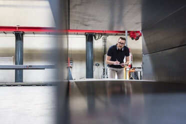 Man writing on clipboard on factory shop floor - DIGF03560