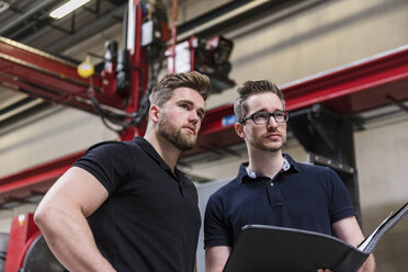 Two men with folder on factory shop floor looking around - DIGF03565