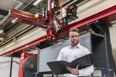 Businessman with folder standing on factory shop floor - DIGF03567