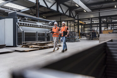 Zwei Männer mit Schutzhelmen und Sicherheitswesten gehen in einer Fabrikhalle - DIGF03582