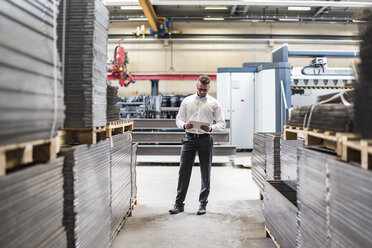 Businessman with tablet standing on factory shop floor - DIGF03585