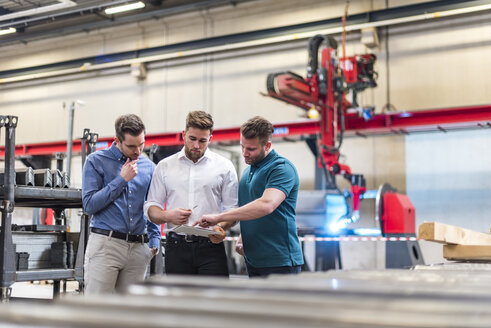 Drei Männer teilen sich ein Tablet in einer Fabrikhalle - DIGF03613