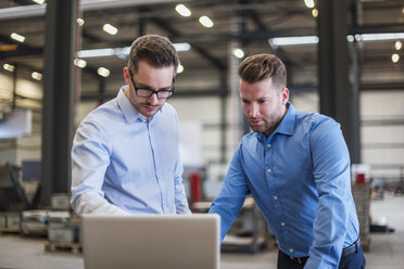 Two businessmen sharing laptop on factory shop floor - DIGF03617