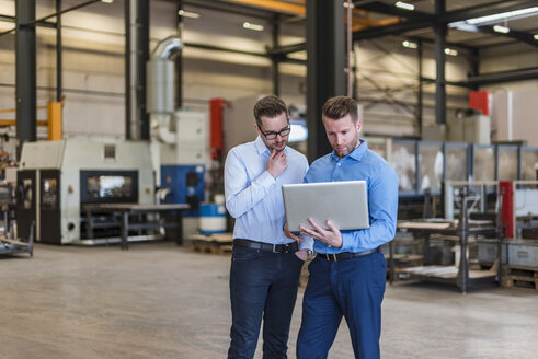 Zwei Geschäftsleute teilen sich einen Laptop in einer Fabrikhalle - DIGF03618