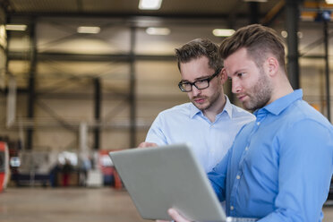 Zwei Geschäftsleute teilen sich einen Laptop in einer Fabrikhalle - DIGF03619