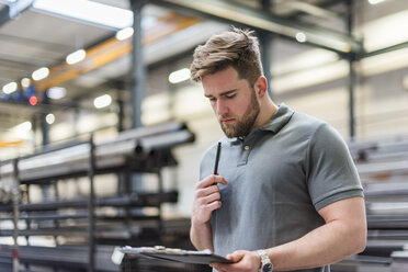 Man writing on clipboard on factory shop floor - DIGF03634