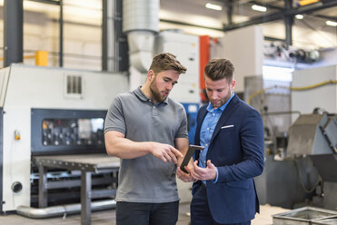 Employee explaining workpiece to businessman on factory shop floor - DIGF03636