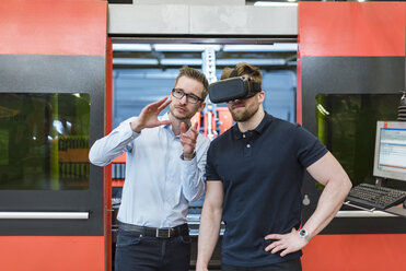 Mann erklärt einem Kollegen mit VR-Brille in einer Fabrik eine Maschine - DIGF03641