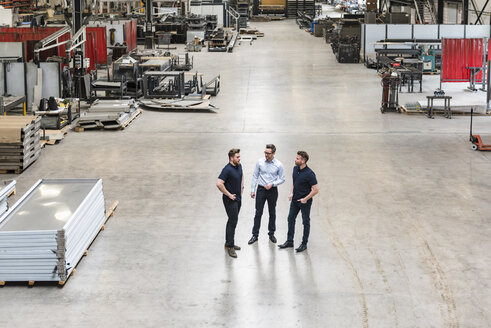 Drei Männer stehen und reden in einer Fabrikhalle - DIGF03648