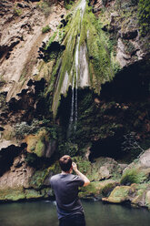 Rückansicht eines männlichen Wanderers mit Blick auf einen Wasserfall über Felsformationen - CAVF31368