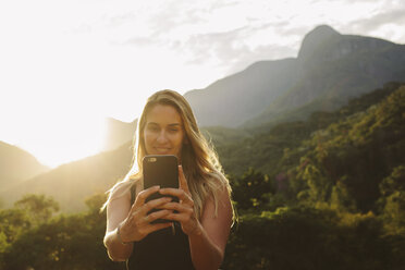 Smiling woman taking selfie while standing against mountains - CAVF31378