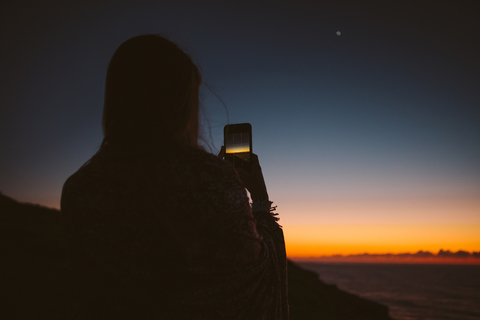 Rückansicht einer Frau, die mit ihrem Smartphone den Sonnenuntergang fotografiert, lizenzfreies Stockfoto