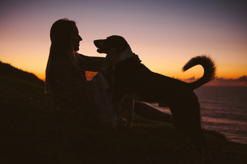 Seitenansicht einer Frau mit Hund auf einem Hügel gegen den Himmel bei Sonnenuntergang - CAVF31384